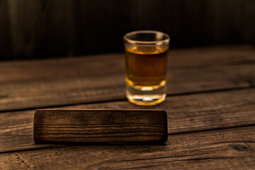 Glass of tequila with the empty wooden plank on an old wooden table. Angle view, focus on the wooden plank