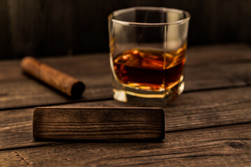 Glass of brandy with cuban cigar and the empty wooden plank on an old wooden table. Angle view, focus on the wooden plank