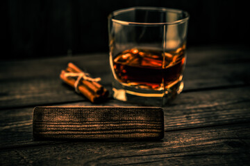Glass of brandy with cinnamon sticks tied with jute rope and the empty wooden plank on an old...