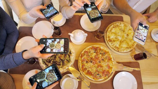 A young group of friends takes pictures of the food on their smartphone before eating it. Selfies with food. A modern group of friends takes photos and videos of food for social media. Fun company