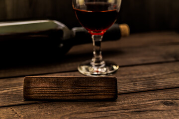 Glass and bottle of red wine with the empty wooden plank on an old wooden table. Angle view, focus on the wooden plank