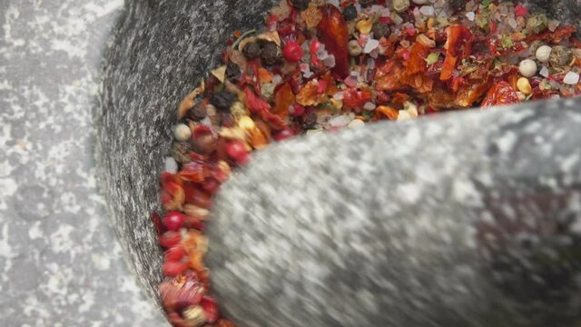 Pestle is grinding various kinds of spices and peppers in the grey stone mortar
