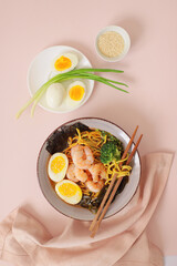 Asian food. Traditional Japanese soup ramen with meat broth, asian noodles, seaweed, eggs and shrimp on pink background.  Asian style food. Top view. Hot tasty ramen soup for dinner.