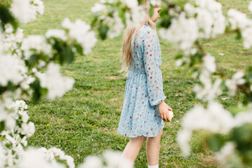 A girl, a teenager in a hat walks in the spring in the city, flowering trees, an apple tree