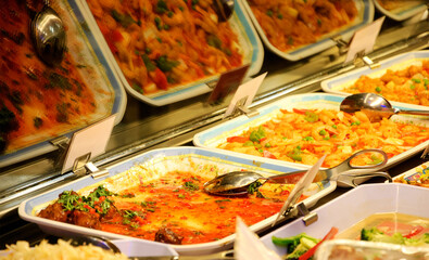 Typical  Asian food diner in Paris (France). Reflection of dishes in glass vitrine. Selective focus on serving tongs.