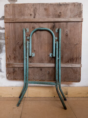 old wooden folding table with blue green painted legs leaning against a wall
