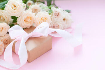 Gift box wrapped in brown paper with pink roses on pink background.