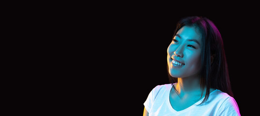 Asian young woman's portrait on dark studio background in neon. Concept of human emotions, facial...