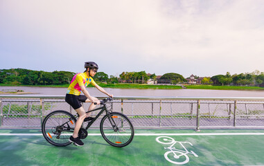 Young Asian healthy cyclist girl wearing helmet cycling and yellow shirt riding bike on bicycle path in the evening, healthy lifestyle concept.
