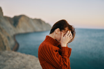 woman in a sweater gestures with her hands outdoors in the mountains near the sea