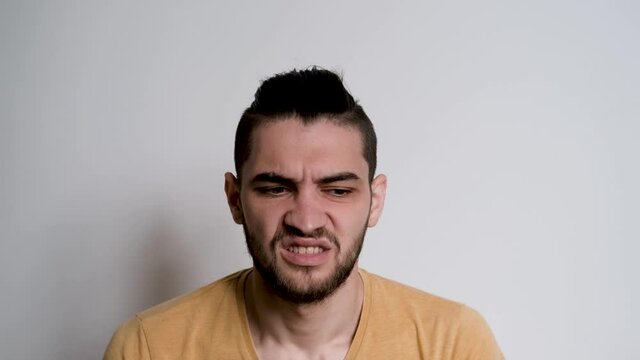 Young Caucasian man with beard makes emotion of disgust with his mouth. Human is excited, confused and does not agree with what is happening, he does not like. Emotions of person in the studio.
