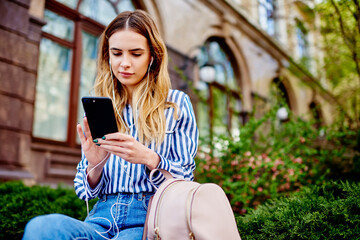 Young woman in earphones using smartphone in campus