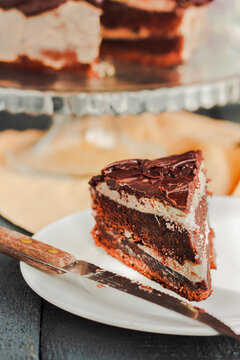 Slice of three chocolate cake ona white plate. Board with delicious tasty homemade cake on table. Blue gray wooden background. Selective focus