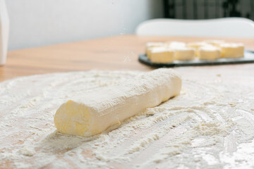 Woman's hands cutting homemade cinnamon roll dough over a floured surface with duster in background. Selective focus with blurred foreground and background