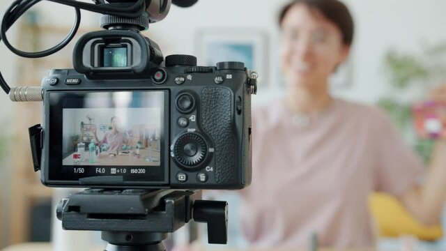 Close-up of video camera with female vlogger recording video about cosmetics on screen. Modern technology and creative social media contect concept.