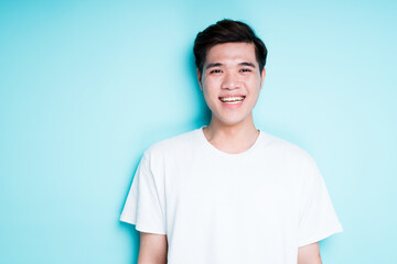 Happy asian in white t-shirt smiling broadly while standing against blue background