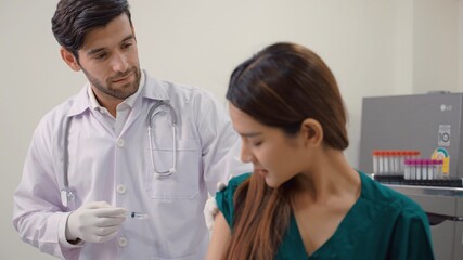 Medical young in safety gloves is making a vaccine injection to a female patient in a health clinic. Doctor uses hypodermic needle and a syringe to put a shot of drug as treatment. Protection, Virus