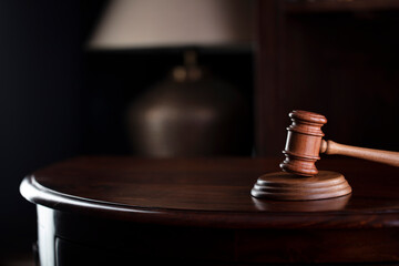 Lawyer office. Gavel on brown shining desk and collection of legal books in the bookshelf.