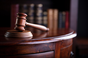 Lawyer office. Gavel on brown shining desk and collection of legal books in the bookshelf.