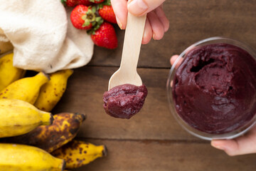 Açai, Hand holding Brazilian frozen açai berry ice cream bowl. with fruits on wooden background. Summer menu top view