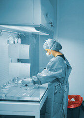 Female scientist working in the fume hood with a mask, cap, gloves and plastic pretreatment gown in...