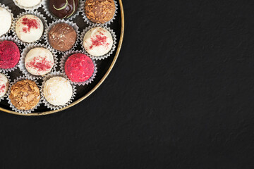 Assorted truffles in a plate on a black background. Homemade candies or energy balls with dried fruits and chocolate. Superfood. Copy space, top view, flat lay.