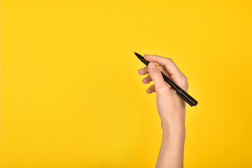 Girl's hand with a pen on a yellow background. Advertising inscription. - obrazy, fototapety, plakaty