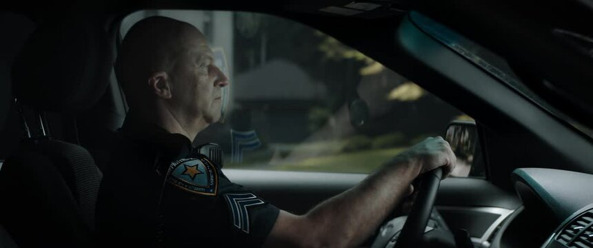 DX Daytime shot of Caucasian American police officer patrolling streets of neighborhood in patrol vehicle. Shot with 2x anamorphic lens