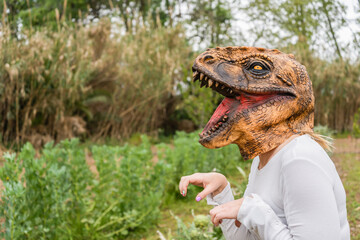 Closeup view of woman with dinosaur head mask in vegetables garden.Copy space