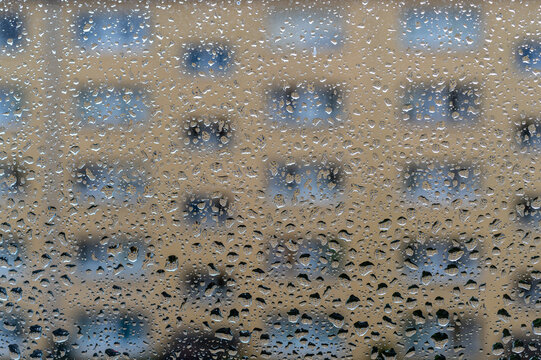szyba z kroplami deszczu i oknami bloku mieszkalnego