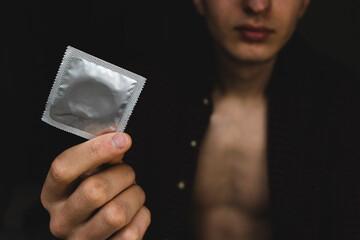 The concept of protection from sexually transmitted diseases, the guy holds a condom in his hand in...