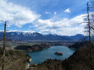 Obraz premium Scenic view of beautiful Bled lake and snow covered peaks of Karavanke mountains in Gorenjska, Slovenia with white clouds on blue sky
