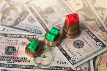 Fototapeta premium Miniature colorful red and green houses on stack coins and dollar banknotes. Finance and property investment concept. Real estate investment.
