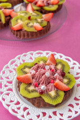 Fruit cake on white plate and pink background. Image from above with fruit tarts in background.
