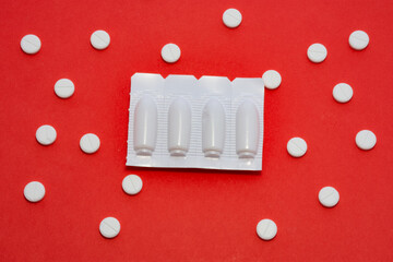 Plastic packaging with vaginal or rectal suppositories is on redbackground surrounded by round tablets that form ornament in polka dots. Concept photo treatment of proctological or gynecological