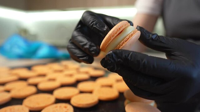 Process Of Making macaroon at home. Shot of hands of female pastry chef holding white macaron with ganache and squeezing red fruit jam from bag. Nature pastry macaroons. High quality 4k footage