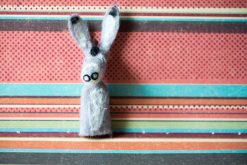a grey donkey finger puppet posing against a colourful background of polka dots and solid stripes
