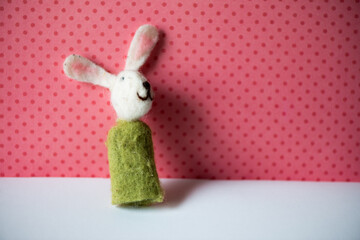 a white rabbit in a green cloak finger puppet posing against red polka dot and pink background