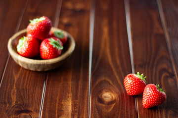Bright red strawberries in a wooden bowl on dark wood; delicious summer berries 