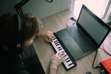 Yong music producer or arranger using laptop, midi keyboard, and other audio equipment to create music at home studio - obrazy, fototapety, plakaty