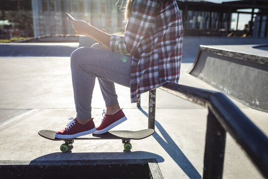 Low section of caucasian woman sitting on handrail with skateboard in the sun