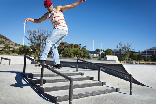 Caucasian man skateboarding on handrail on sunny day