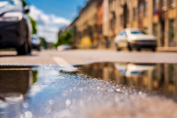 Sunny day after the rain in the city, parked on the street cars on the background of the facades of the house. Close up view from the level of the puddle on the pavement