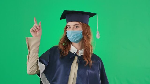 diploma online, graduate in medical mask rejoices at received certificate of education and points her fingers up during distance learning green screen background, chroma key