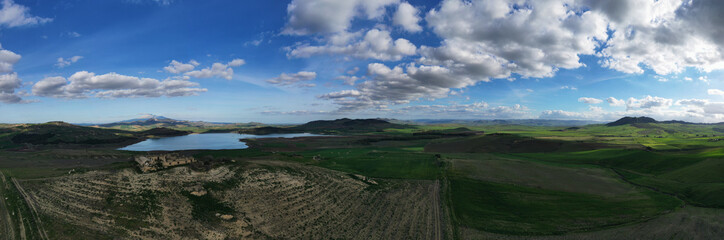 Fototapeta na wymiar 180 degree aerial photo of Ogliastro lake in the heart of Sicily with Etna view. Place of great naturalistic value surrounded by hills planted with cereals. A destination for migratory bird species.