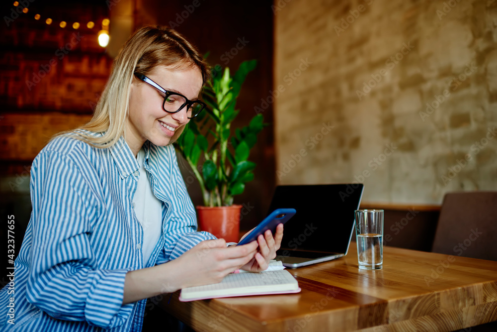 Poster millennial female student in classic spectacles browsing web publication on cellphone device using c