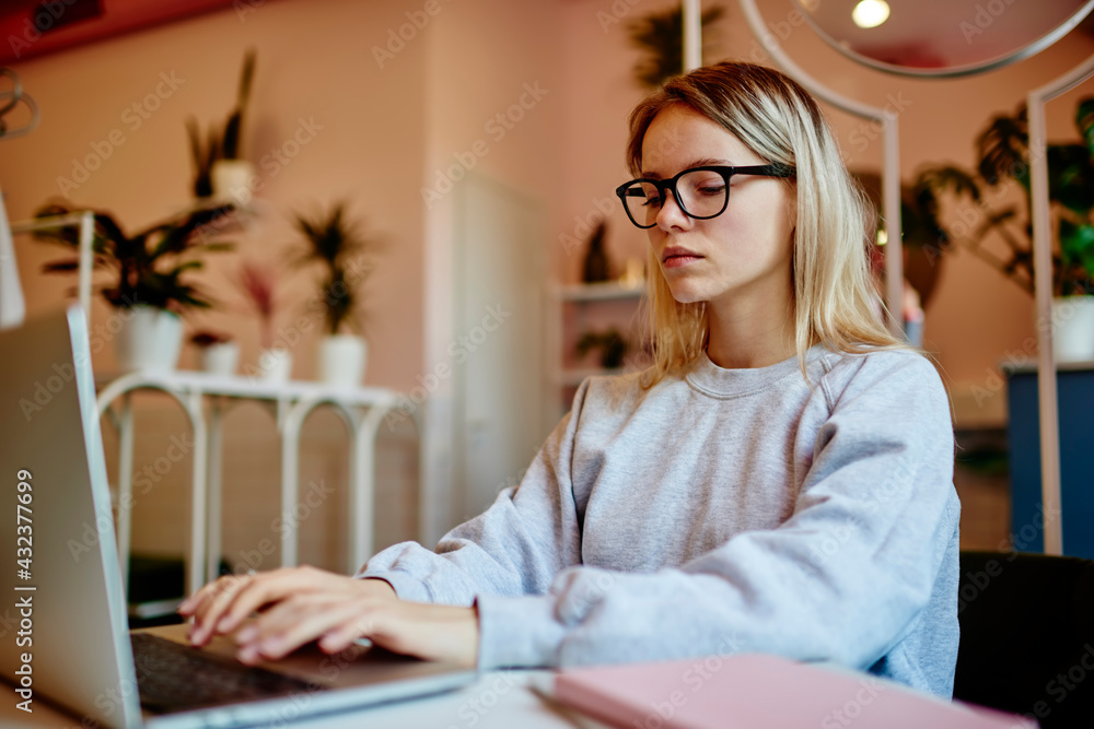 Poster skilled hipster girl in spectacles browsing web page while making online wireless booking, millennia