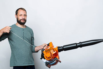 A man operating Engine pull cord a Air Blower Tool. Starting a handheld leaf blower, cordless, electric leaf blower isolated on grey background. Garden and lawn care concept. Studio shot