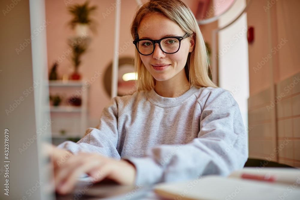 Poster portrait of attractive hipster girl in optical spectacles looking at camera while doing distance job