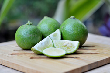 three limes (Citrus × aurantiifolia) with slices on a wooden tray. commonly used in tropical...